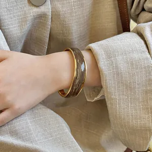 Dettaglio di un bracciale rigido dorato con smalto ondulato marrone su fondo in lino.