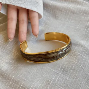 Dettaglio macro di un bracciale a fascia dorato ondulato con smalto effetto marmo