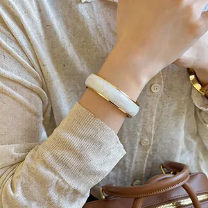 Elegante bracciale rigido aperto con bordo dorato, effetto marmo bianco e motivo a onde