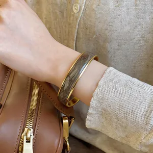 Primo piano di un bracciale dorato con smalto grigio ondulato indossato al polso