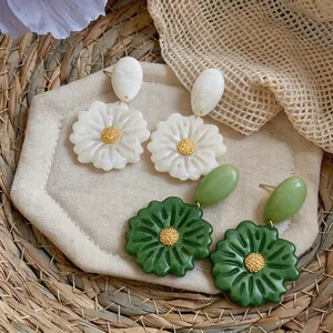 Grandi orecchini pendenti a fiore in resina bianco e verde su sfondo di paglia rustico