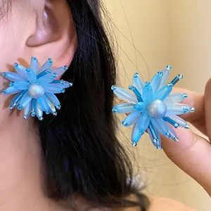 Dettaglio di orecchini a fiore in vetro blu con perla, stile francese raffinato.