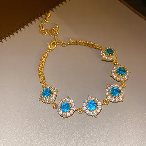 Gros plan d'un bracelet doré élégant avec cinq breloques fleurs en zircon bleu radiant