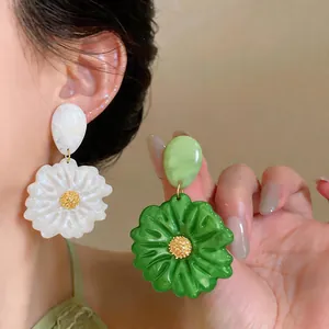 Primo piano di orecchini a fiore in resina bianca e verde con centri dorati testurizzati.