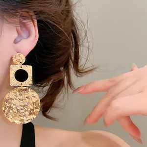 Close-up detail showing the texture of oversized gold hammered geometric drop earrings