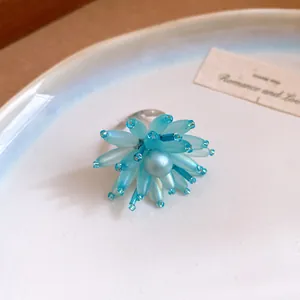 Dettaglio macro di un elegante anello a fiore in vetro blu con perla su un piatto bianco