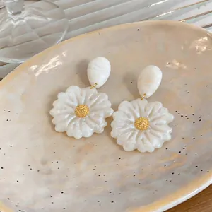 Dettaglio di orecchini a lobo a forma di fiore in resina bianca con centro dorato.