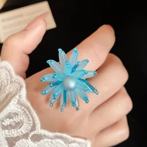 Primo piano di un anello a fiore in perle di vetro blu mare su un dito con pizzo bianco
