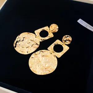 Detailed macro shot of 18k gold plated hammered geometric drop earrings on velvet.