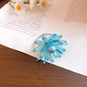 Macro dettaglio di un anello a fiore con petali di vetro blu mare e perla su carta d'epoca.