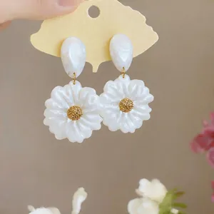 Primo piano di orecchini a forma di fiore in resina bianca con centro dorato su cartoncino