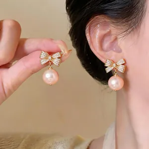 Detaillierte Nahaufnahme eleganter goldener Zirkonia-Schleifenohrringe mit rosa Perlen
