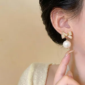 Detailansicht eines eleganten Zirkon-Schleifen-Ohrrings mit Perle am Ohr getragen