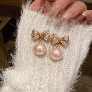 Detailansicht eleganter goldener Schleifenohrringe mit Zirkonia und rosa Perlenanhängern