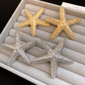 Macro detail of vintage gold and silver textured starfish earrings on a gray velvet tray.
