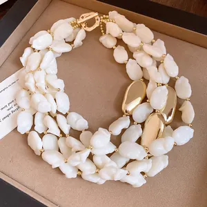 Detailed macro view of multi-strand white acrylic bead necklace with gold OT buckle