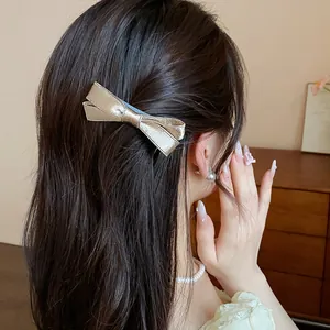 Elegant champagne gold satin bow hair clip displayed on model dark hair detail view