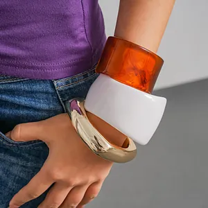 Close-up detail of chunky resin and gold-tone geometric bangles worn on a model's wrist