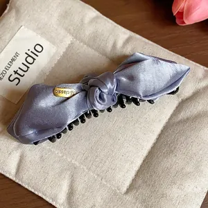 Detail view of an elegant purple satin bow hair claw clip on a textured cream pouch
