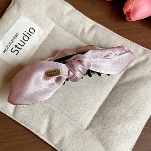Macro detail of a pink satin bow hair clip showing smooth fabric texture and gold tag