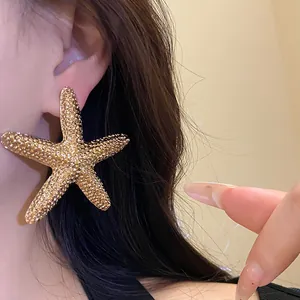 Detailed view of oversized gold textured starfish stud earring worn on ear with hair background