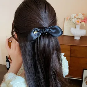 Detail shot of a black satin bow hair clip worn on long dark wavy hair in a cozy room.