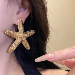 Close-up of a large textured gold starfish stud earring worn on model's ear