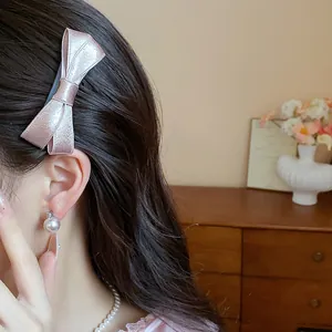 Close-up detail showing the texture of a pink satin bow hair clip on dark wavy hair