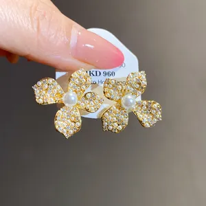 Close-up detail of elegant gold flower stud earrings featuring white pearls and shiny zircons.