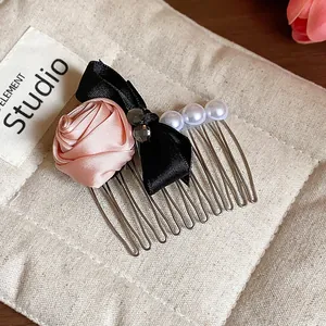 Macro view of an elegant pink satin rose hair comb featuring a black bow and white pearls