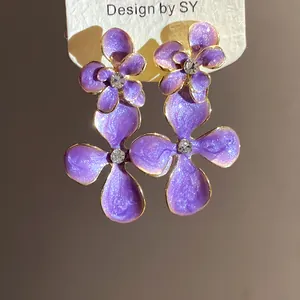 Close-up detail of purple enamel flower drop earrings with a sparkling crystal center