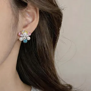 Detailed close-up of a colorful flower-shaped earring with pearls and zircon stones on ear