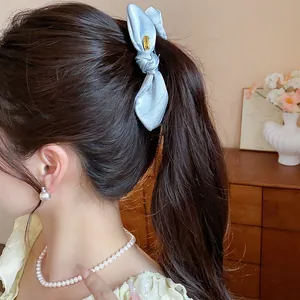 Close-up of a light blue satin bow hair clip worn by a woman with a pearl necklace