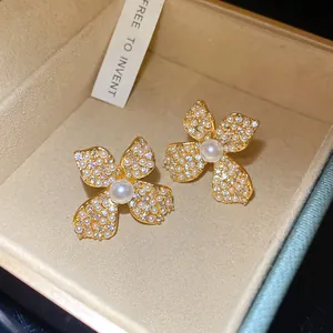 Elegant gold flower stud earrings with shimmering pearls and zircon stones detail.