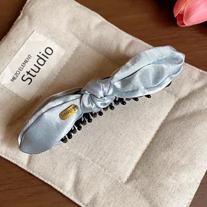 Detail shot showing the texture of light blue satin bow hair clip on beige pouch