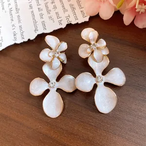 Elegant white enamel flower drop earrings with rhinestones on vintage wood background