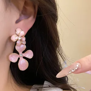 Macro view of elegant pink flower pendant earrings with rhinestones worn on an ear.