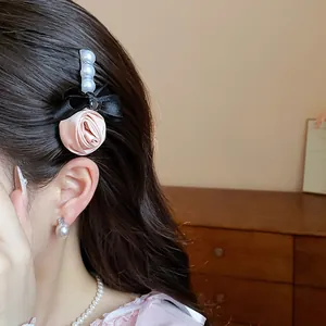 Detailed view of pink fabric rose and black satin bow hair clip with white pearls