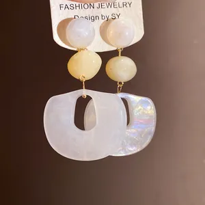 Macro detail of white and yellow acrylic oval drop earrings with silver needle posts.
