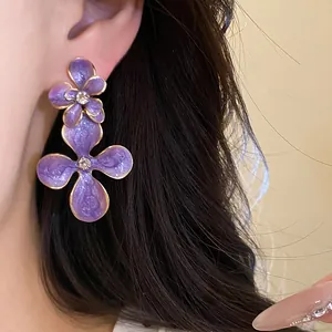 Close-up of purple enamel flower earrings with crystal centers on model's ear.