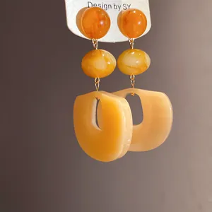 Macro detail view of elegant amber acrylic three-tier drop earrings with silver needle