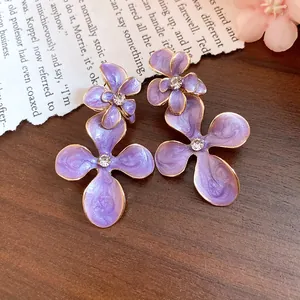 Detail view of purple enamel flower earrings with central rhinestones on a wooden background.