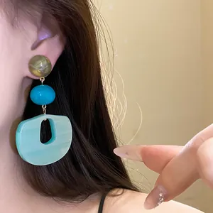 Close-up view of elegant layered geometric acrylic drop earrings worn by a model's ear.