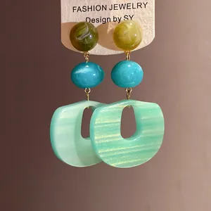 Close-up of mint green acrylic pendant earrings with layered marbled beads.