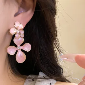Close-up of pink enamel flower drop earrings with clear rhinestones on a silver needle.