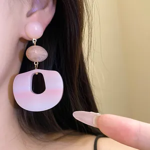 Macro view of elegant pink gradient acrylic pendant earrings worn by a female model