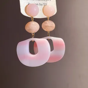 Close-up of pink gradient acrylic pendant earrings with marble texture beads