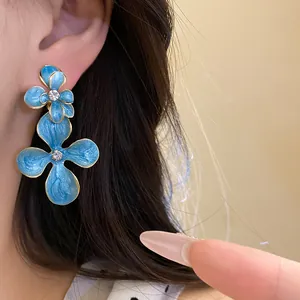 Detailed view of vintage-style blue enamel floral drop earrings with crystals worn on ear