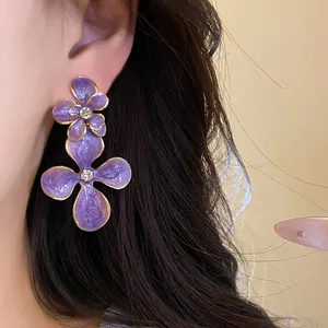 Detailed close-up of purple enamel flower drop earrings with rhinestones on a model's ear