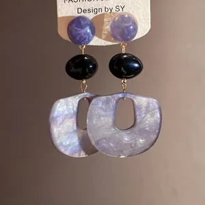 Close-up of stylish acrylic drop earrings with purple marbled and black resin beads.